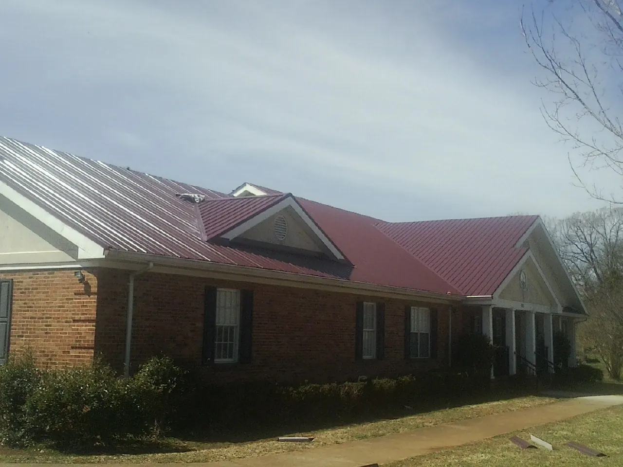 Red metal roof with gabled entries on a long brick building, from a Hail Damage Roof Repair job in Takoma Park