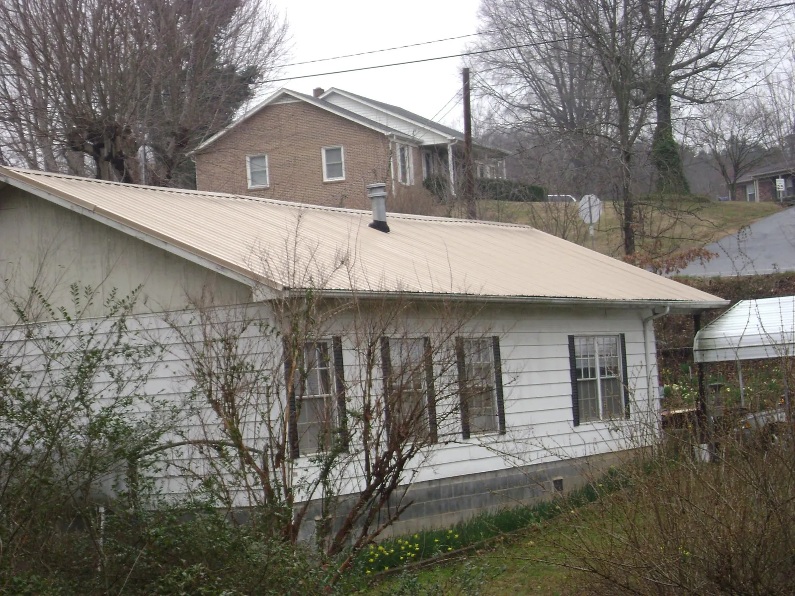 Tan metal roof on a white sided house set into a hillside — Commercial Roofing by Roofing Brothers in Takoma Park